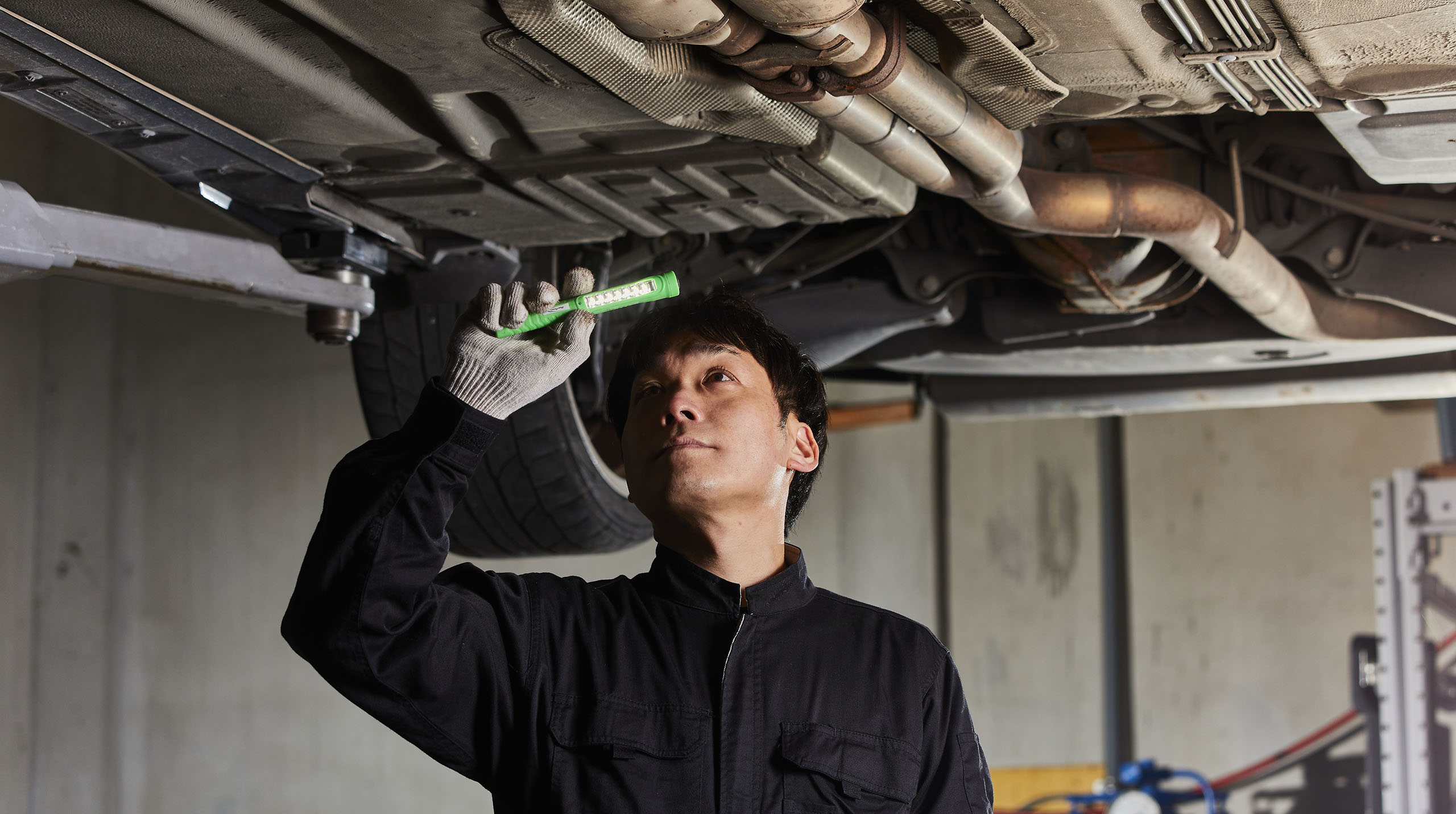 車体の底の点検のために目を光らせる。普段は見えないところにも安全を守るポイントがある。 防錆効果のある『ボディーアンダークリアコーティング』を施工して腐食を防ぐことも。
